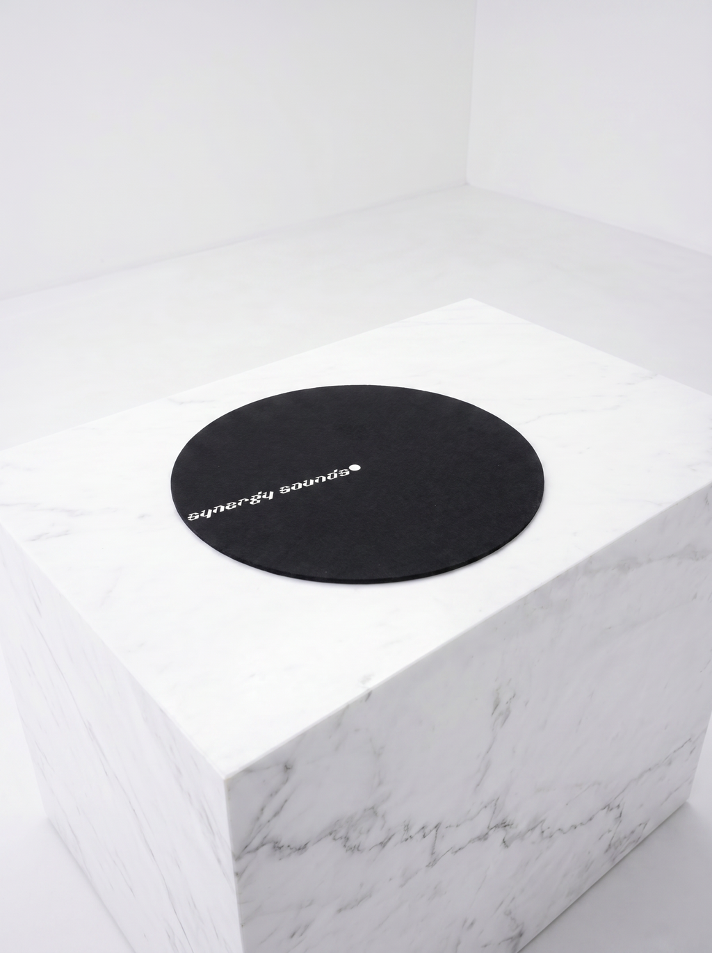 Round black mat with 'synergy sounds' logo on a white marble surface