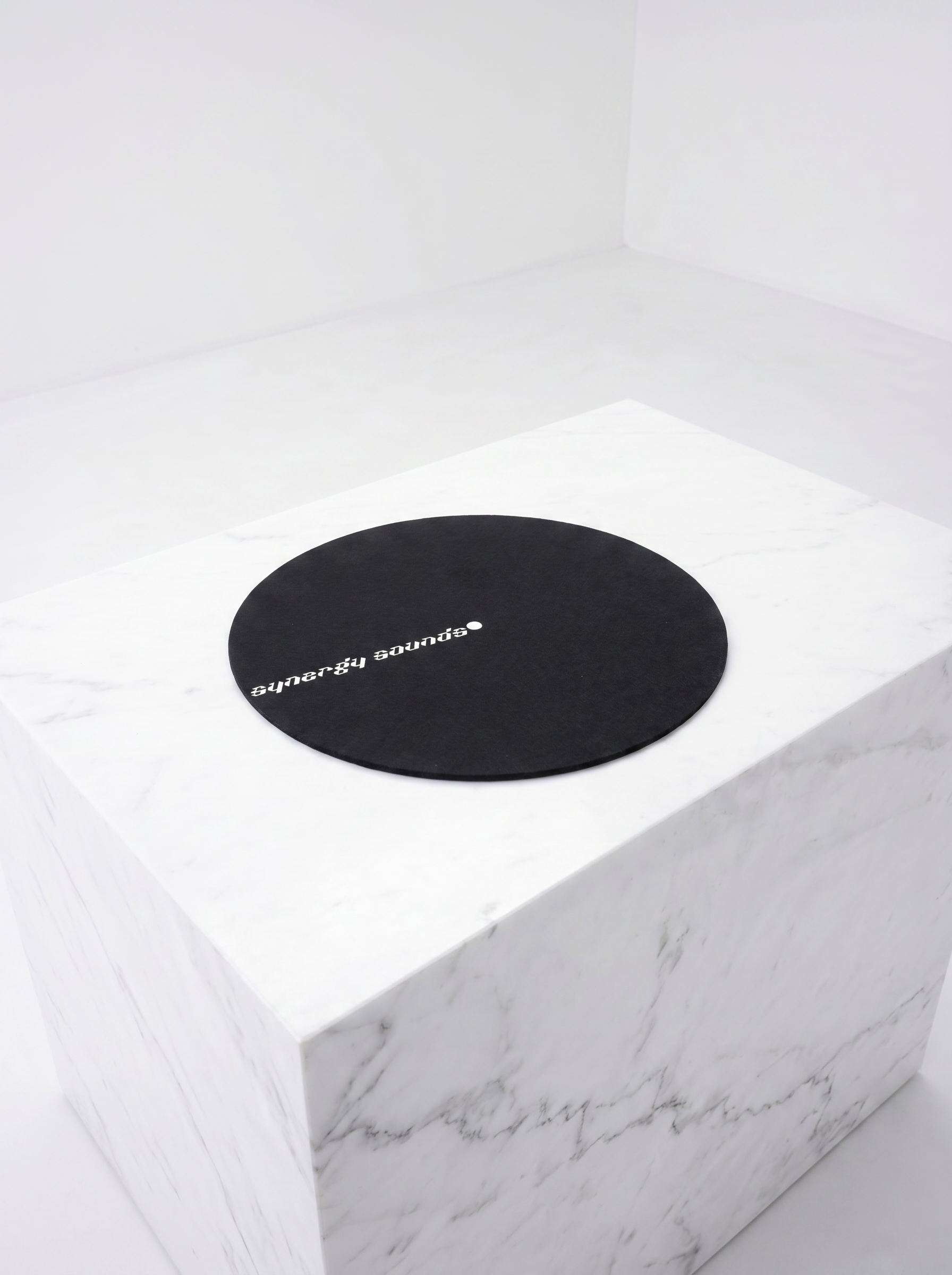 Round black mat with 'synergy sounds' logo on a white marble surface