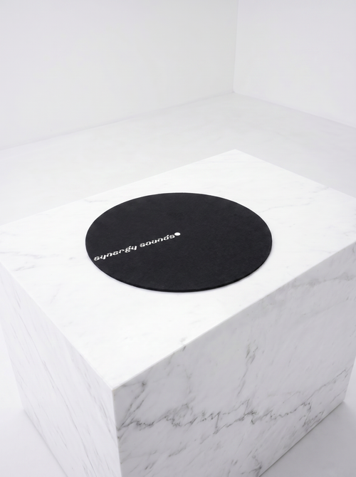 Round black mat with 'synergy sounds' logo on a white marble surface